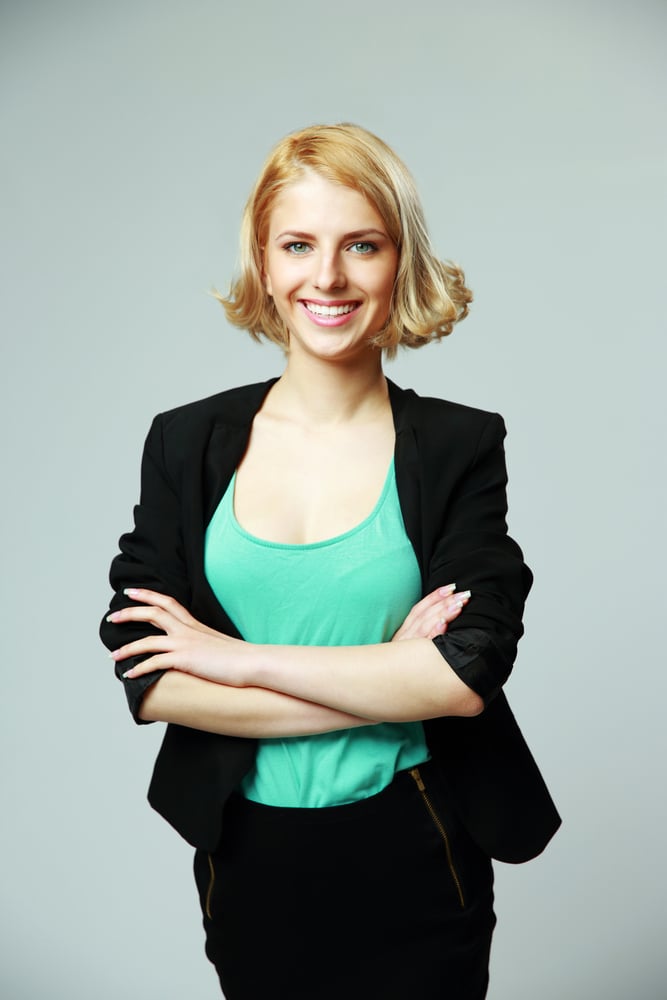 Portrait of a young happy woman with arms folded on gray background