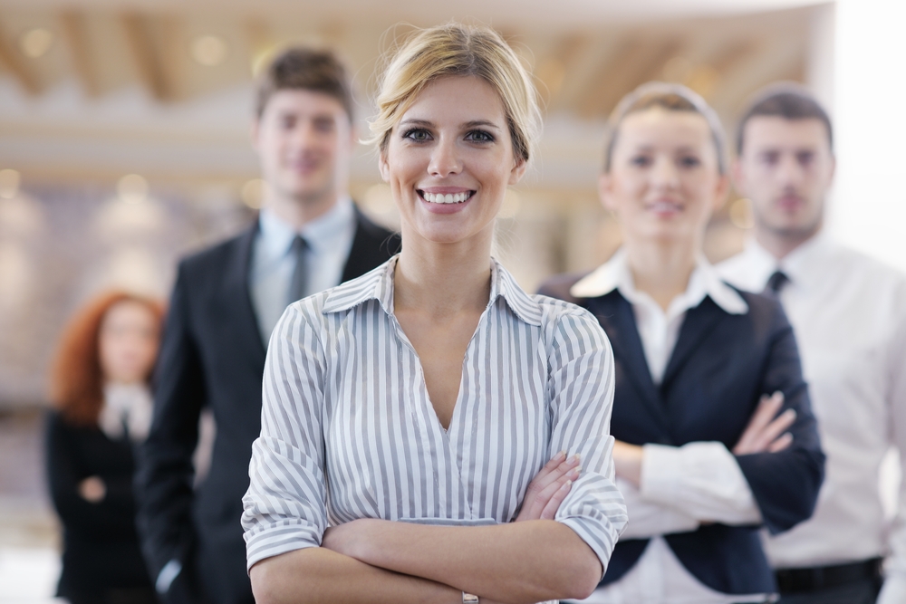 business woman standing with her staff in background at modern bright office conference room